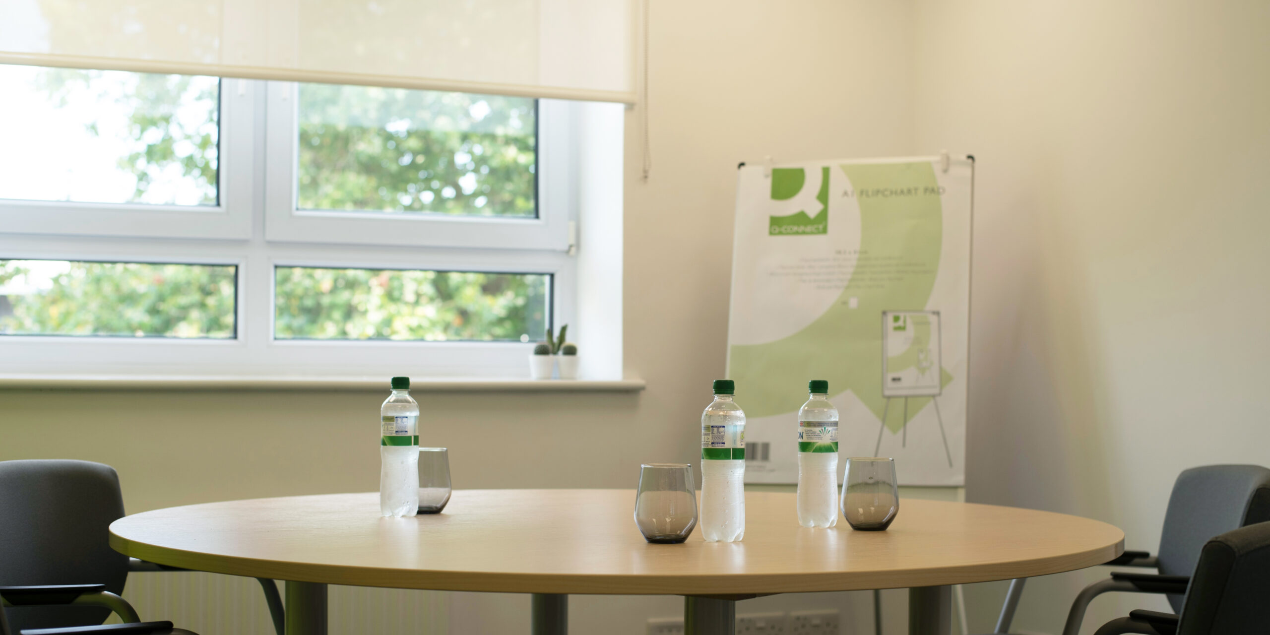 Round table with water and glasses.  FLipchart paper next to the window. 