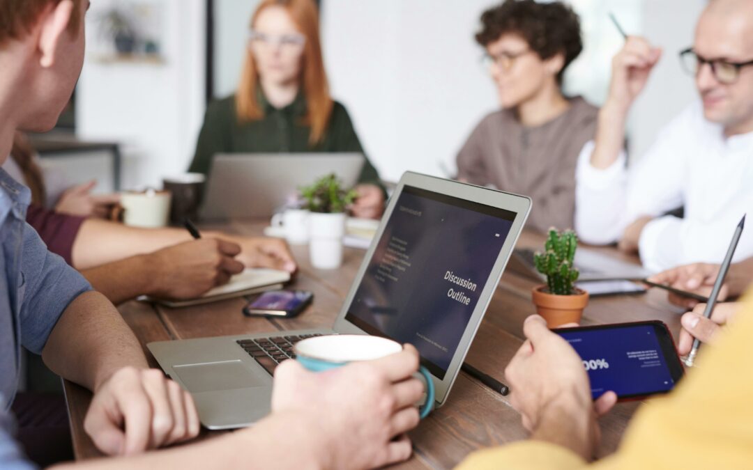 Group of people sat around a table with laptops having a meeting.